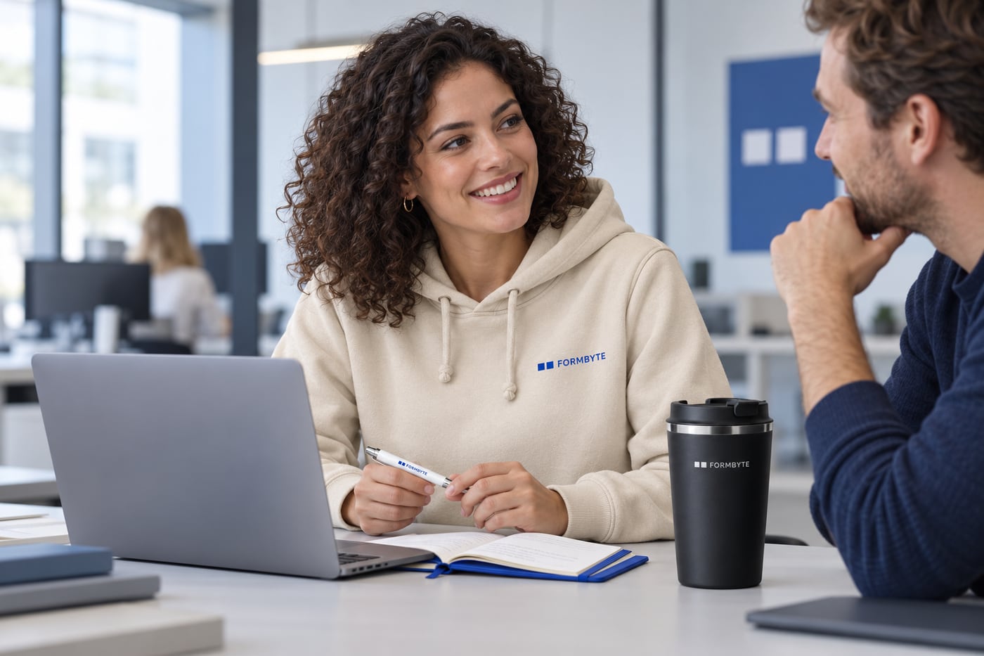 Medarbetare på kontor med FORMBYTE-hoodie och anteckningsbok, exempel på produkter med eget varumärke